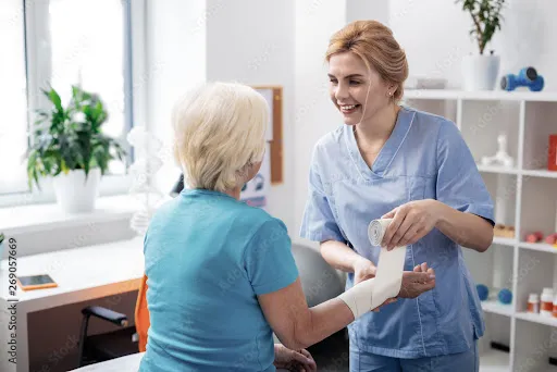 An elderly woman is being bandaged by a caretaker.